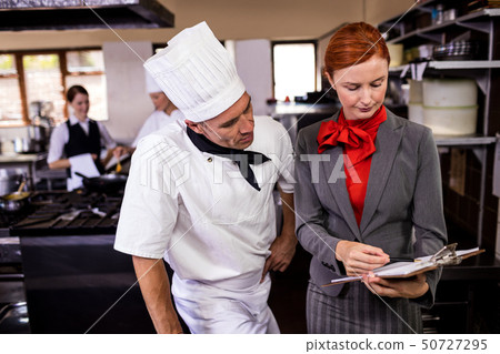 Female manager and male chef writing on clipboard in kitchen 50727295