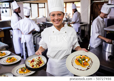Female chef holding plate of prepared pasta in kitchen Female chef holding plate of prepared pasta in kitchen 50727498