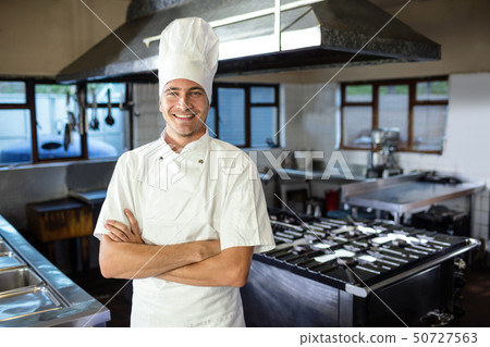 Male chef standing with arms crossed in kitchen 50727563