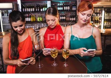 Female friends using mobile phone while enjoying wine 50727614