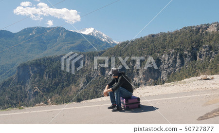 Young man sitting on purple suitcase sunny day Young man sitting on purple suitcase sunny day 50727877