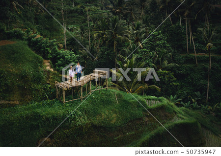 Couple standing on wooden bridge near rice terraces in Bali Indonesia. Holding hands. Romantic mood 50735947
