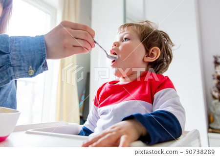 mother feeds a little toddler boy with a spoon during lunch mother feeds a little toddler boy with a spoon during lunch 50738289