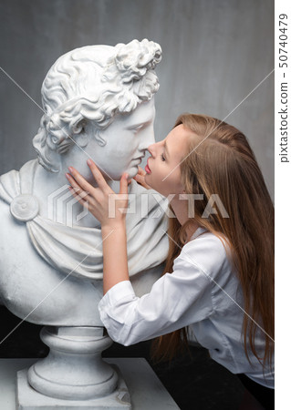 Young woman kissing God Apollo bust sculpture. Ancient Greek god of Sun and Poetry Plaster copy of a Young woman kissing God Apollo bust sculpture. Ancient Greek god of Sun and Poetry Plaster copy of a 50740479