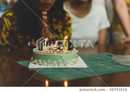 Shot in low light woman blowing on candles on birthday cake with friends. Shot in low light woman blowing on candles on birthday cake with friends. 50741018