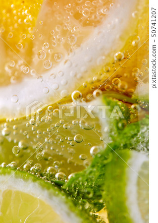 Green leaf of mint, pieces of lemon and lime with bubbles in a transparent glass. Macro photo of 50741207