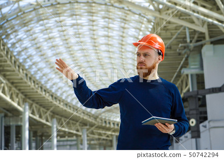 A man in a helmet in a large space with a tablet A man in a helmet in a large space with a tablet 50742294