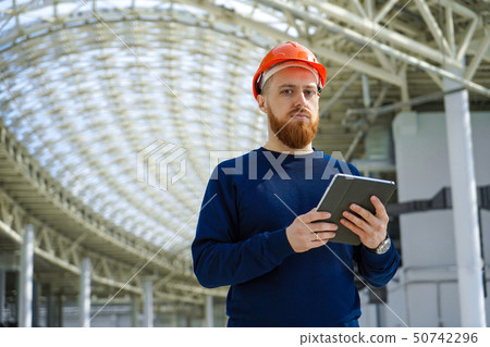A man in a helmet in a large space with a tablet A man in a helmet in a large space with a tablet 50742296