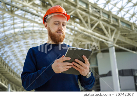A man in a helmet in a large space with a tablet A man in a helmet in a large space with a tablet 50742307