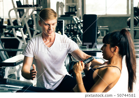 Young Caucasian male personal trainer at gym, supporting female fitness client 50744581