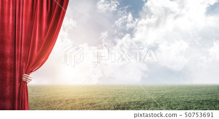 Green meadow behind red curtain and hand holding it Green meadow behind red curtain and hand holding it 50753691