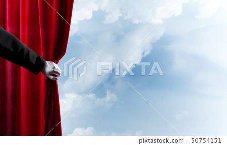Cloudy landscape behind red curtain and hand holding it Cloudy landscape behind red curtain and hand holding it 50754151