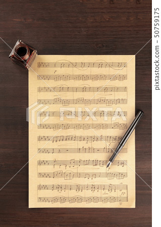A piece of sheet music, shot from above on a dark rustic wooden background with a nib pen and an ink 50759175