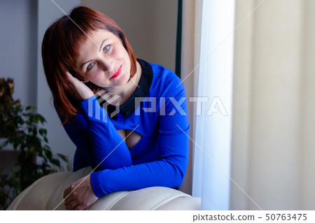 Beautiful woman in a blue dress on a leather white armchair in the room Beautiful woman in a blue dress on a leather white armchair in the room 50763475