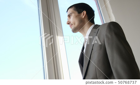 Young successful businessman standing in front of windows looking into distance on the city 50768737