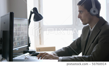 Successful businessman in headphones sitting at his desk, working on a computer by the panoramic Successful businessman in headphones sitting at his desk, working on a computer by the panoramic 50768914