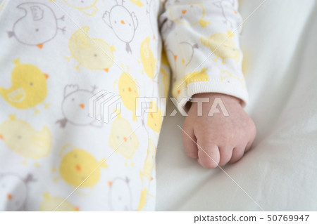 A baby in a yellow pajamas is asleep with his fist clenched on a white quilt. A baby in a yellow pajamas is asleep with his fist clenched on a white quilt. 50769947