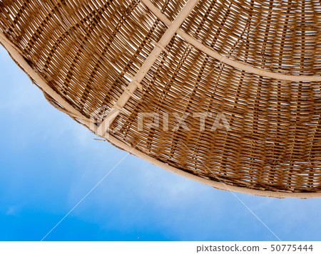 Closeup image of part of straw umbrella protecting from sun on the beach against blue sky. Pefect 50775444