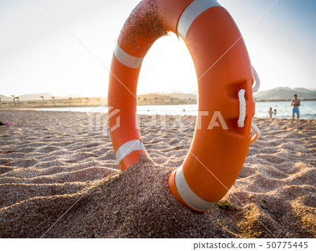 Closeup photo of red plastic life saving ring on sand of the sea beach against beautiful sunset over 50775445