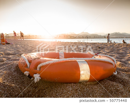 Closeup image of red plastic life saving ring on sandy sea beach at sunset light 50775448
