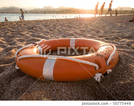 Closeup photo of red plastic life saving ring on sand of the sea beach against beautiful sunset over 50775449