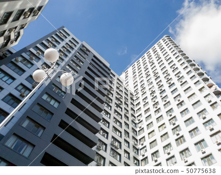 View from the ground on roof tops of modern multistored living building against blue sky and bright 50775638