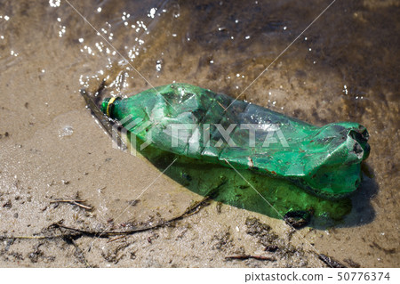 Plastic bottle of green color in a pond on a muddy beach Plastic bottle of green color in a pond on a muddy beach 50776374