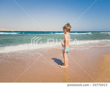 Toned image of 3 years old toddler boy standing on the sea beach and looking at horizon. Child Toned image of 3 years old toddler boy standing on the sea beach and looking at horizon. Child 50778413