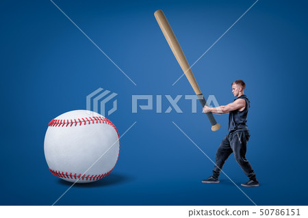 Side view of young athletic man in gym suit, holding enormous bat and ready to hit huge baseball. Side view of young athletic man in gym suit, holding enormous bat and ready to hit huge baseball. 50786151