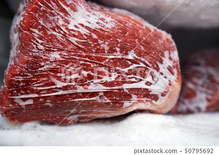 Large pieces of red meat in a freezer with a big quantity of frozen ice and snow 50795692