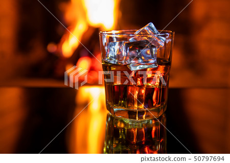 Glass of whiskey with ice near the fireplace 50797694