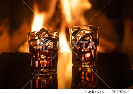 Glass of whiskey with ice near the fireplace 50797695