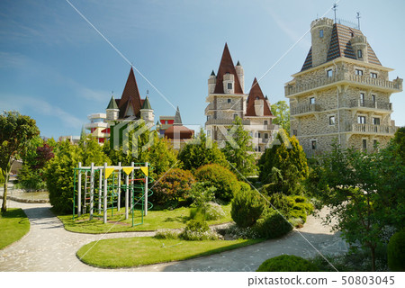 modern Victorian-style luxury hotel with a small children's play area at the foot, against a blue 50803045