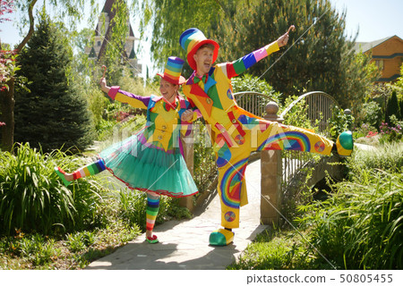 couple of funny clowns, a guy and a girl in a beautiful summer park, on a background of greenery couple of funny clowns, a guy and a girl in a beautiful summer park, on a background of greenery 50805455