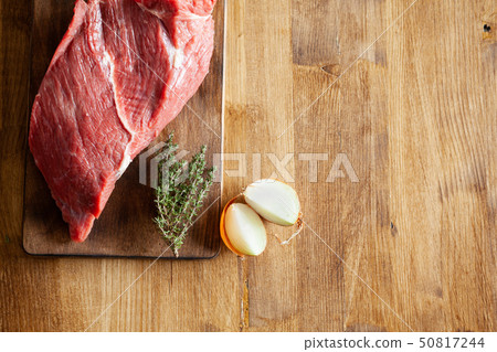 Top view of white onions next to a big chunk of red meat on wooden table 50817244