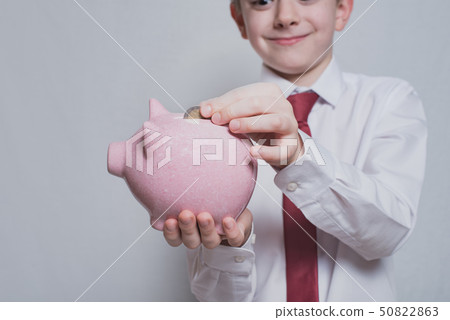 Smiling boy puts a coin in a pink piggy bank. Smiling boy puts a coin in a pink piggy bank. 50822863