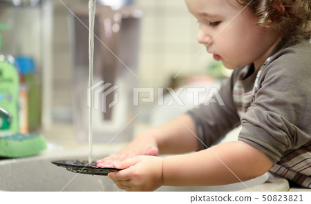 Little child is washing dishes in kitchen Little child is washing dishes in kitchen 50823821