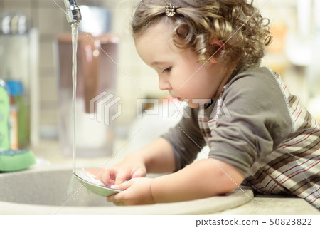 Little child is washing dishes in kitchen Little child is washing dishes in kitchen 50823822