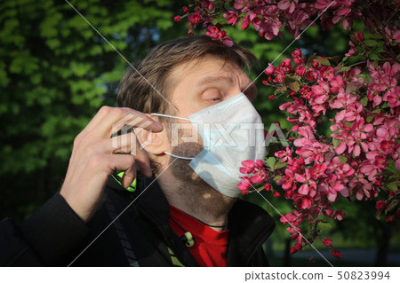 A man in a medical mask sneezes from pollen. A man in a medical mask sneezes from pollen. 50823994