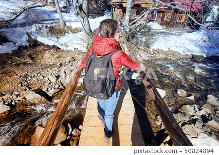 A happy girl, with a red jacket and a black backpack, crossing a wooden bridge A happy girl, with a red jacket and a black backpack, crossing a wooden bridge 50824894
