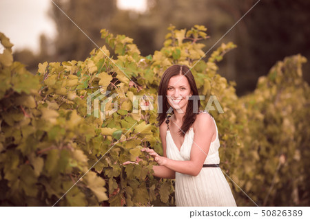Smiling woman in white dress standing in vineyard Smiling woman in white dress standing in vineyard 50826389