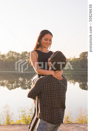 Romantic, people and summer concept - man raised a woman in his arms near the lake at the sunset Romantic, people and summer concept - man raised a woman in his arms near the lake at the sunset 50826636