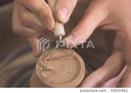 Master removes the top layer of clay on pot with a special tool. Master removes the top layer of clay on pot with a special tool. 50830462