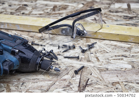 Power drill with goggles for eye safety and building level against the background of OSB panel 50834702
