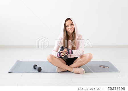 Healthy lifestyle, people and sport concept - Smiling woman sitting on yoga mat and drinking water 50838696