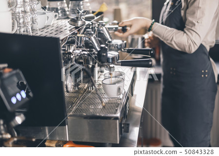 Coffee pouring into the cups while barista standing near 50843328