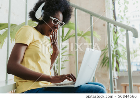 Low angle of young African lady wearing modern white headphones and eyeglasses Low angle of young African lady wearing modern white headphones and eyeglasses 50844566