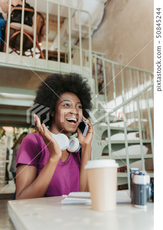 Waist up of excited African woman with headphones having chat on smartphone Waist up of excited African woman with headphones having chat on smartphone 50845244