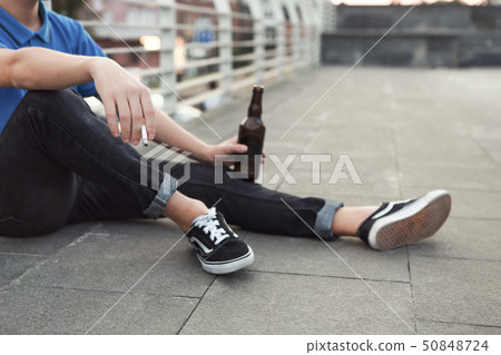 Teen guy smoking cigarette and drinking beer, sitting alone Teen guy smoking cigarette and drinking beer, sitting alone 50848724