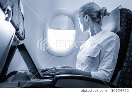 Attractive caucasian female passenger looking through the plain window while working on modern Attractive caucasian female passenger looking through the plain window while working on modern 50854723